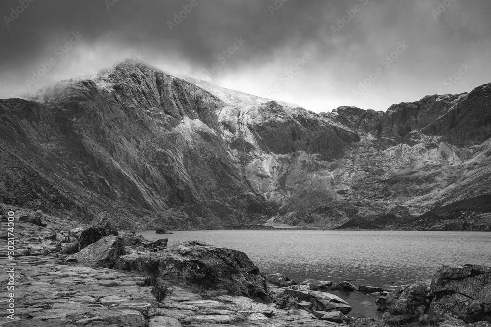 Beautiful moody Winter landscape image of Llyn Idwal and snowcapped Glyders Mountain Range in Snowdonia in black and white