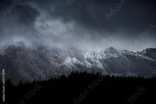 Stunning dramatic landscape image of snowcapped Glyders mountain range in Snowdonia during Winter with menacing low clouds hanging at the peaks photo