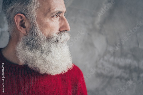 Cropped closeup photo of serious aged guy looking side empty space minded wear red knitted pullover cool hipster santa outfit isolated concrete grey wall background