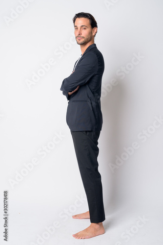 Full body shot profile view of Hispanic businessman looking at camera with arms crossed