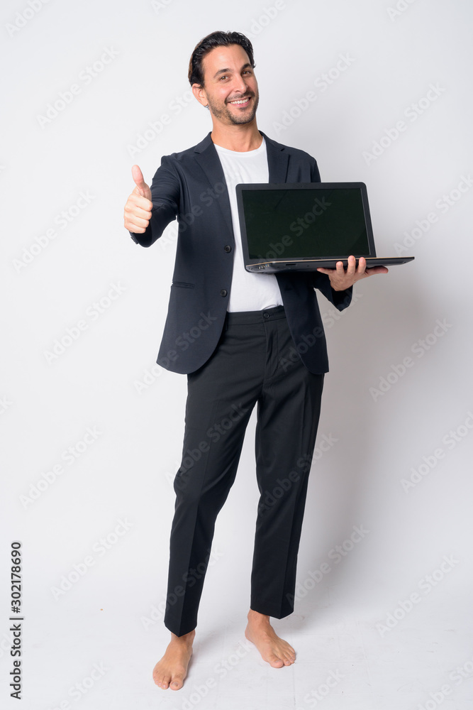 Full body shot of happy Hispanic businessman showing laptop and giving thumbs up Full body shot of happy Hispanic businessman showing laptop and giving thumbs up