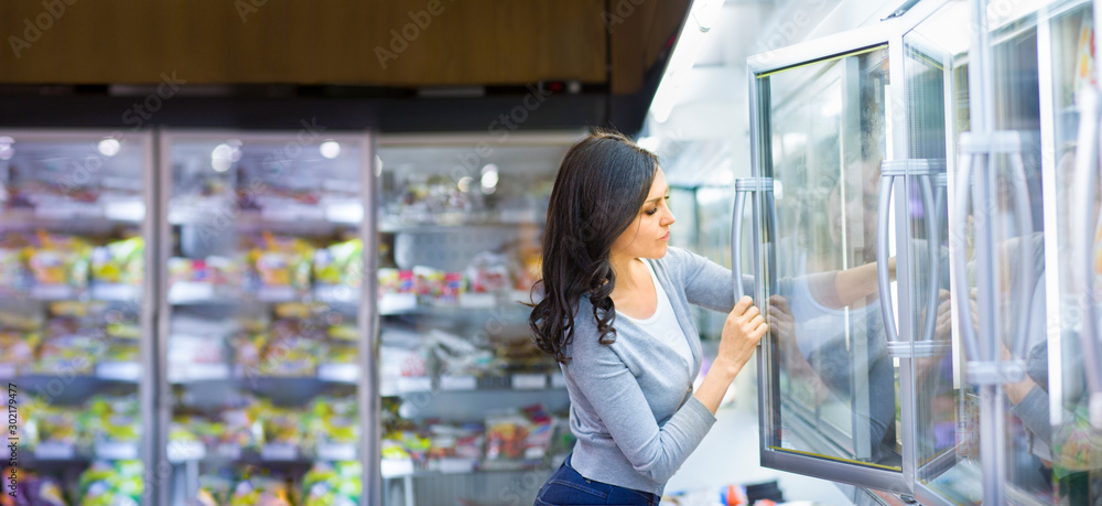 Fototapeta premium Woman choosing a dairy products at supermarket. Reading product information