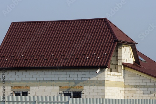 part of a gray brick house with a brown tiled roof against a blue sky