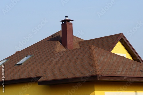 house roof with brown tiles and metal chimney against a blue sky