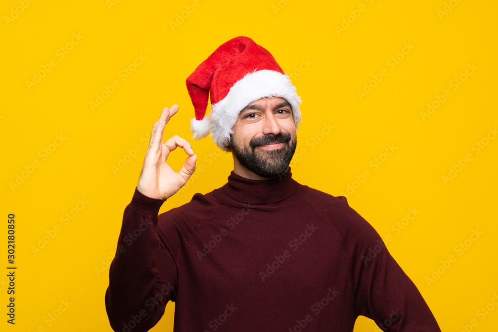 Man with christmas hat over isolated yellow background showing ok sign with fingers Man with christmas hat over isolated yellow background showing ok sign with fingers