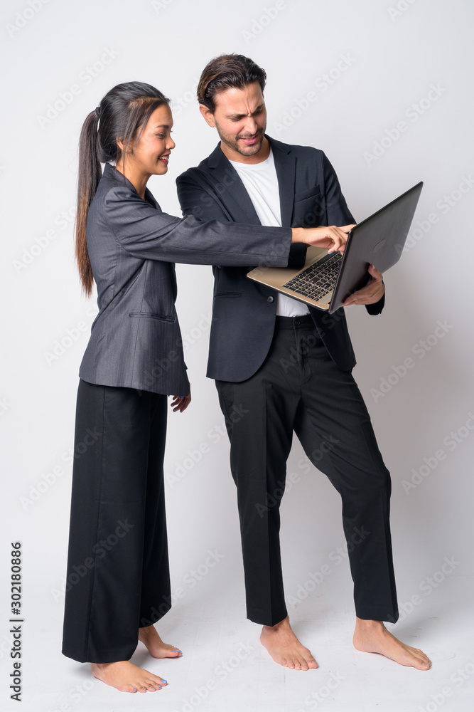Full body shot of happy multi ethnic business couple working with laptop together Full body shot of happy multi ethnic business couple working with laptop together