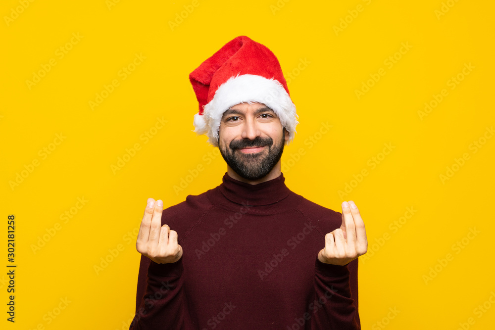 Man with christmas hat over isolated yellow background making money gesture Man with christmas hat over isolated yellow background making money gesture
