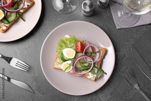Tasty sandwich with ham and quail eggs served on grey table, flat lay