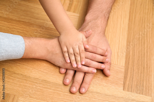 Happy family holding hands on wooden background, closeup