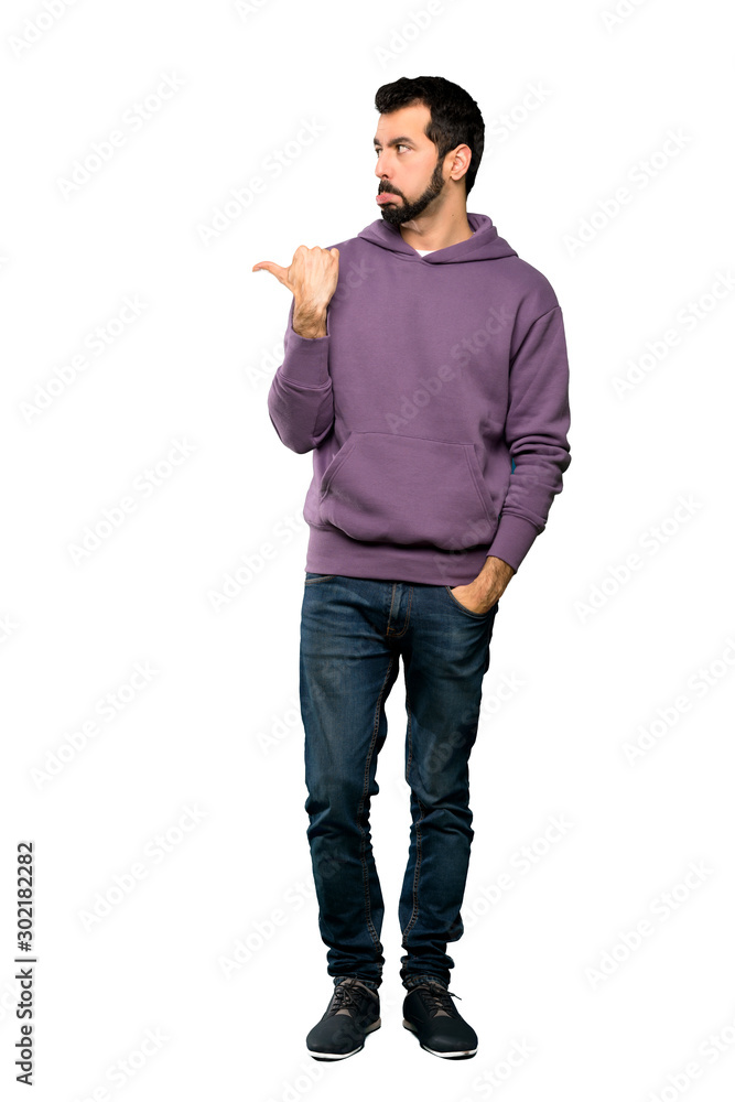 Full-length shot of Handsome man with sweatshirt unhappy and pointing to the side over isolated white background Full-length shot of Handsome man with sweatshirt unhappy and pointing to the side over isolated white background