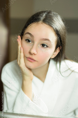 Beautiful teenage girl looks in reflection of the mirror in bathroom healthy skin of face with cotton disk