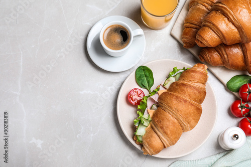 Flat lay composition with tasty croissant sandwich on light grey marble table, space for text