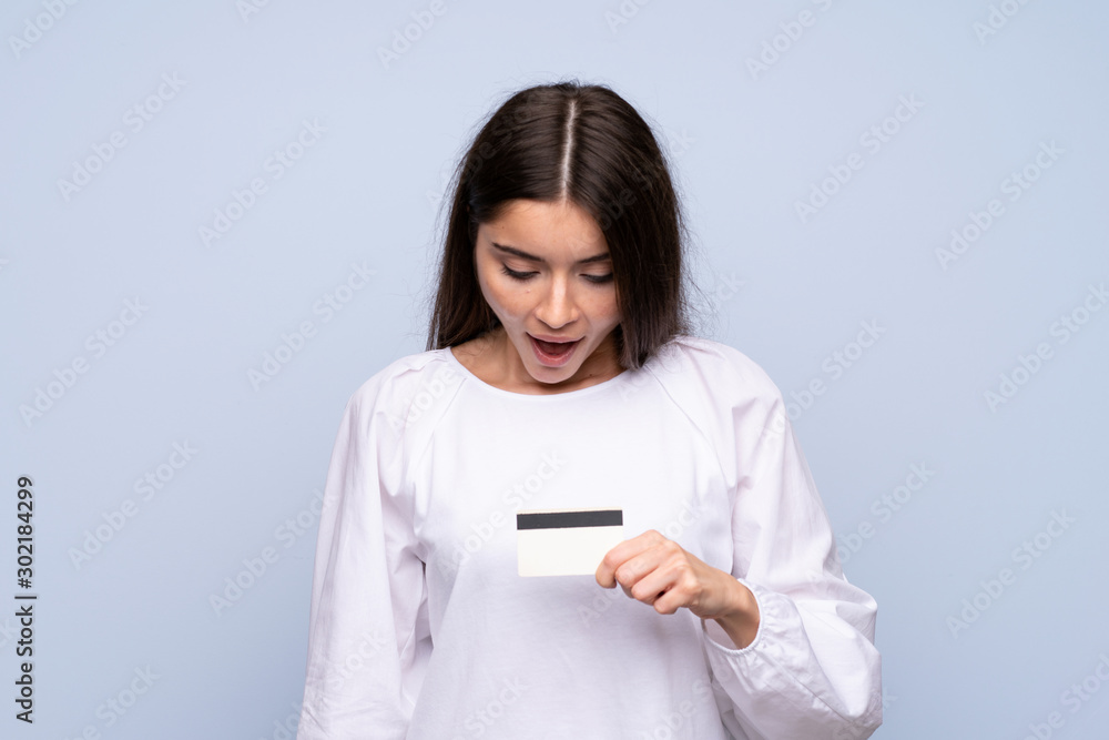 Young woman over isolated blue background holding a credit card Young woman over isolated blue background holding a credit card