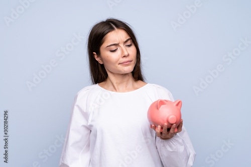 Young woman over isolated blue background holding a big piggybank