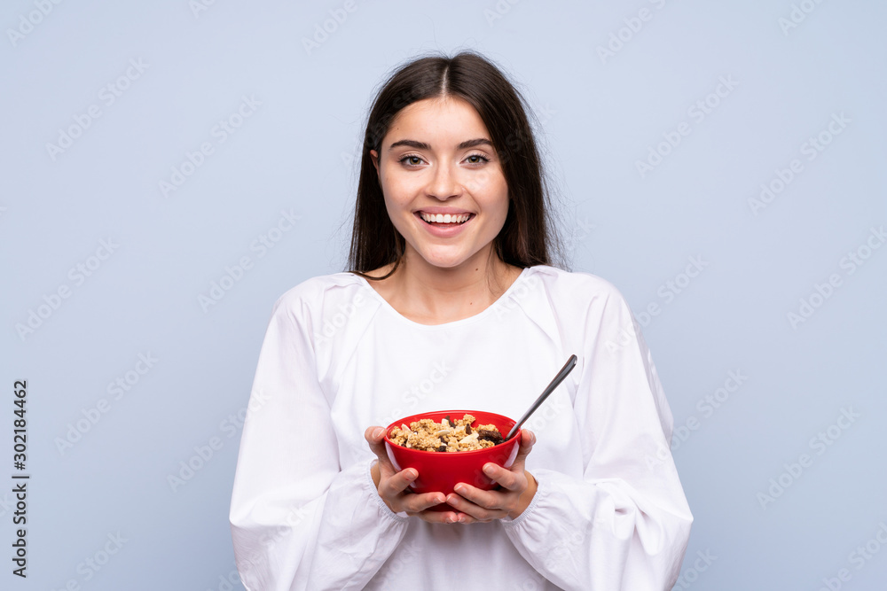 Young woman over isolated blue background holding a bowl of cereals Young woman over isolated blue background holding a bowl of cereals