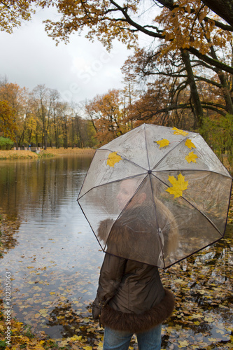 woman under a transparent umbrella on autumn day on the river shore..