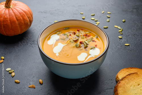 Healthy organic pumpkin cream soup with cream, croutons, seeds and basil on a dark wooden background