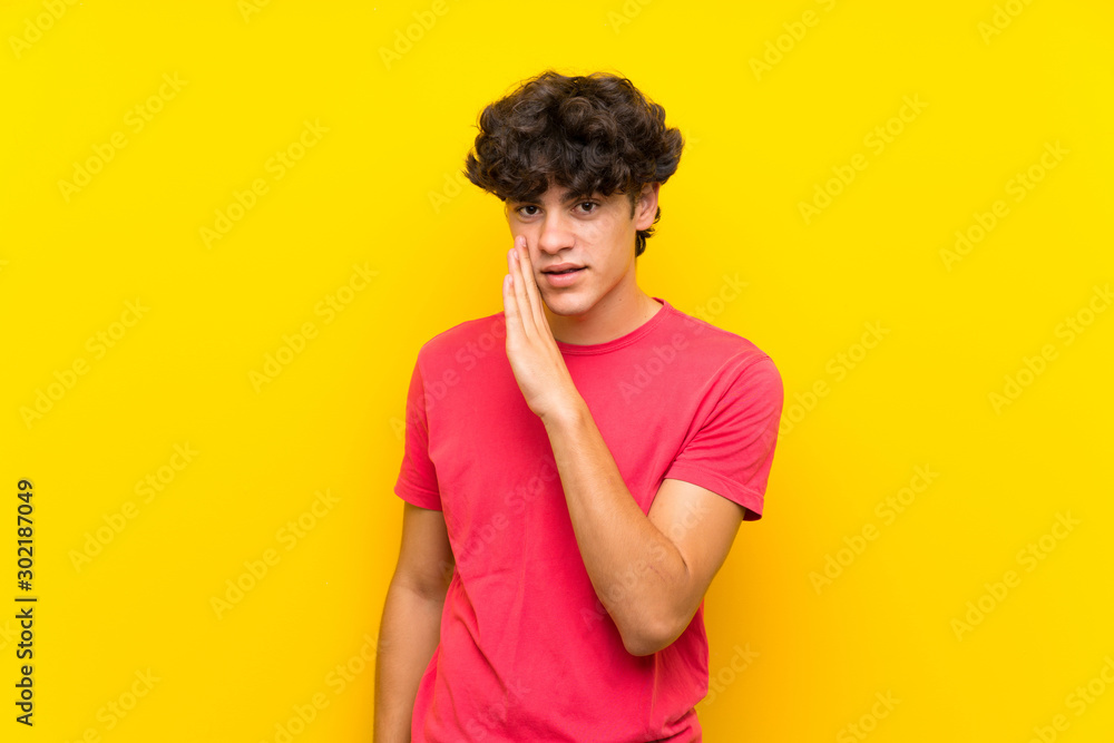 Young man over isolated yellow wall whispering something Young man over isolated yellow wall whispering something