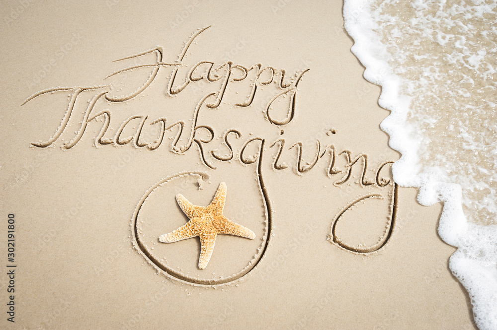 Happy Thanksgiving message handwritten on smooth sand beach with decorative starfish and oncoming wave - obrazy, fototapety, plakaty 