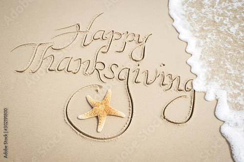 Happy Thanksgiving message handwritten on smooth sand beach with decorative starfish and oncoming wave