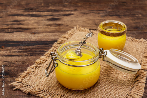 Pure or desi ghee (ghi), clarified melted butter. Healthy fats bulletproof diet concept or paleo style plan. Glass jar, silver spoon on vintage sackcloth. Wooden boards background photo