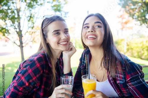 Two young women drinking juice and lemonade in the park