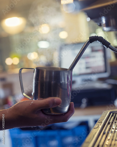 Steaming milk jug barista's hand coffee machine preparing cappuccino latte cafe restaurant