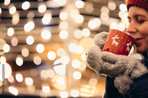 Christmas light and a woman holding in hand a red mug with hot drink