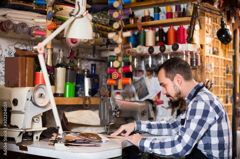 male worker sewing stitches on belt in leather workshop