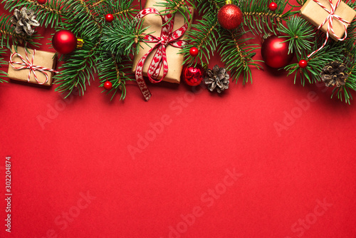 Christmas composition made of fir branches, gift boxes, red holiday decorations on red background
