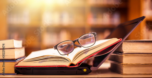 Book in library with old open textbook, stack piles of literature text archive on reading desk, and aisle of bookshelves in school study class room background for academic education learning concept photo