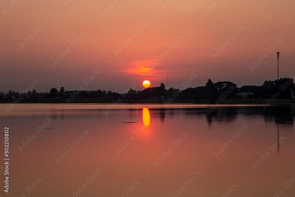 Landscape of the sunset over the tree and reflaction water in the canal at sisaket province , Thailand. The sun is falling on the horizon and reflecting water.