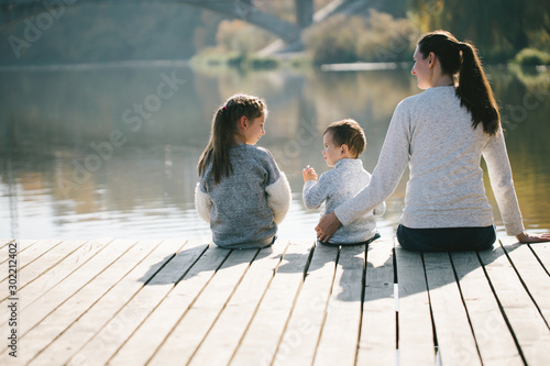 Mother and children relaxing next to a lake. They are smiling and talking on a sunny autumn day