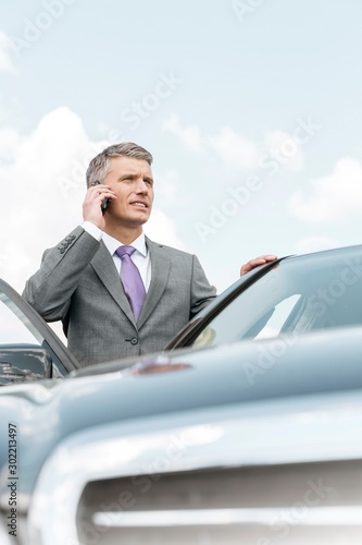 Businessman talking on smartphone outside the car