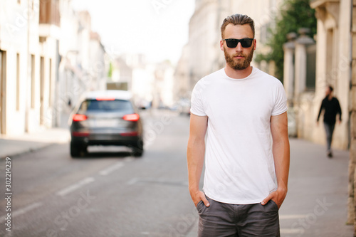 Hipster handsome male model with beard wearing white blank t-shirt with space for your logo or design in casual urban style