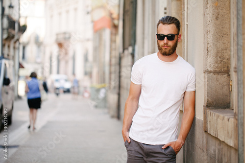 Hipster handsome male model with beard wearing white blank t-shirt with space for your logo or design in casual urban style