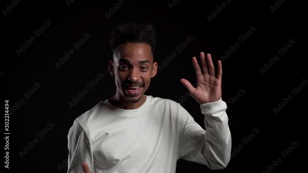 Young african american man smiling and dancing in excellent mood isolated on black studio wall. Slow motion. Young african american man smiling and dancing in excellent mood isolated on black studio wall. Slow motion.