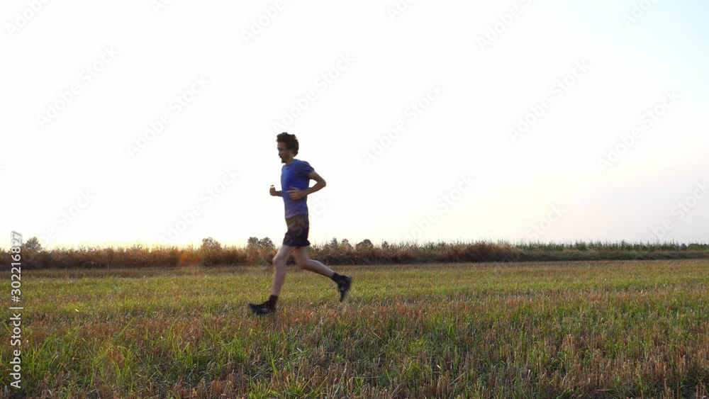 Slow motion of sporty man running in a field at sunset Slow motion of sporty man running in a field at sunset