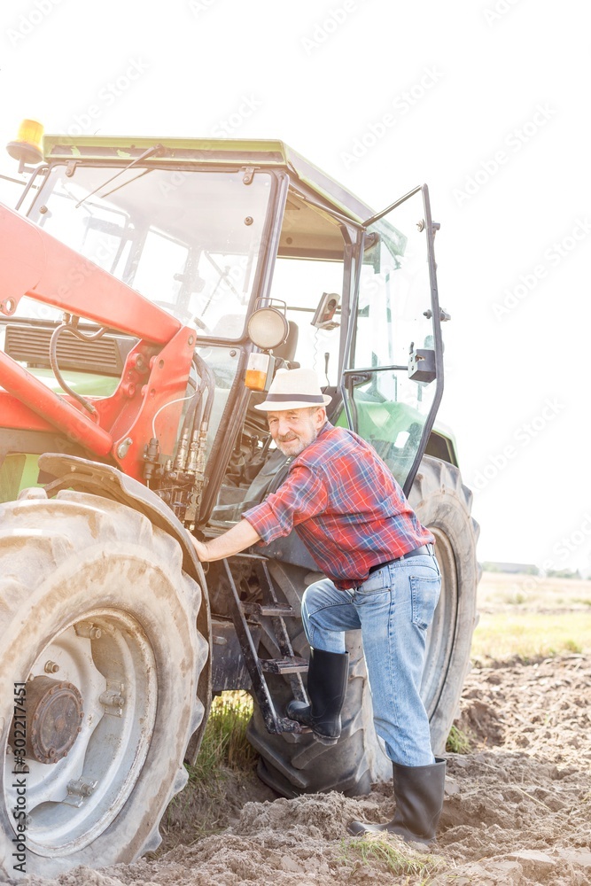 Senior farmer hopping on to drive tractor in field