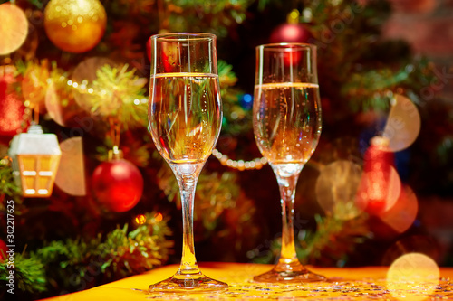 Two glasses of champagne on the background of a beautifully decorated balls, garlands, stars Christmas tree. Around the glow of rays and bokeh lights
