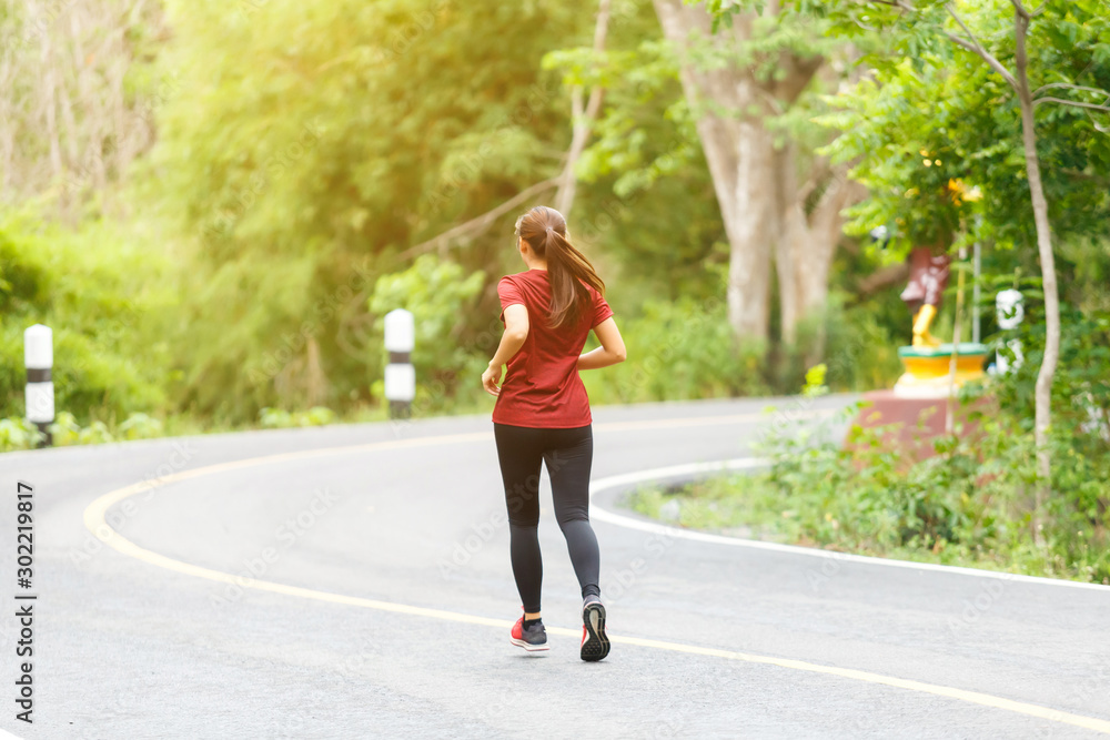 Back of woman runner and runing at the road surround with green forest.