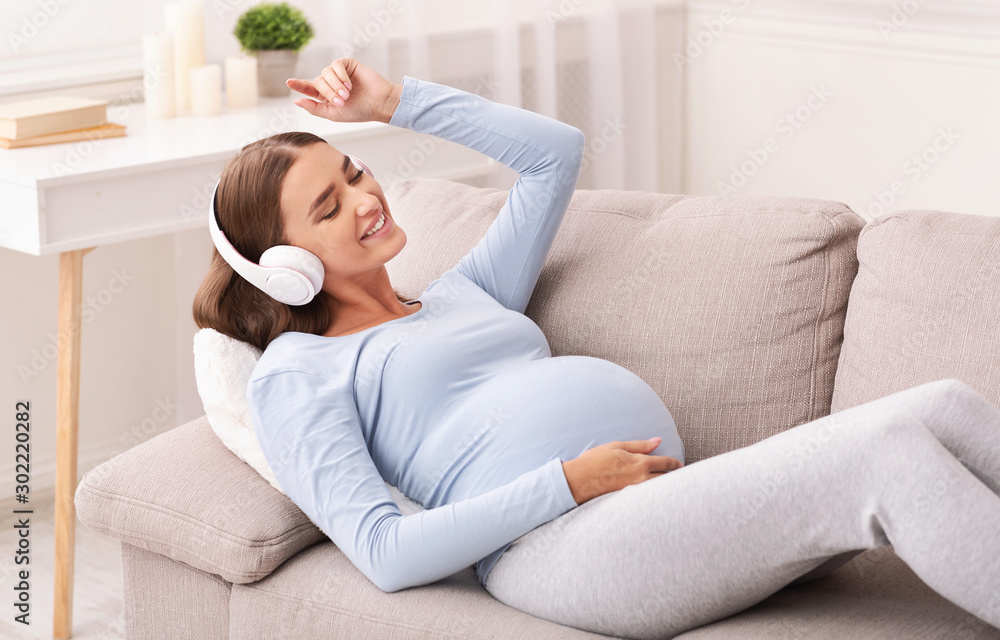 Happy Expectant Girl In Earphones Enjoying Music Lying On Sofa Happy Expectant Girl In Earphones Enjoying Music Lying On Sofa