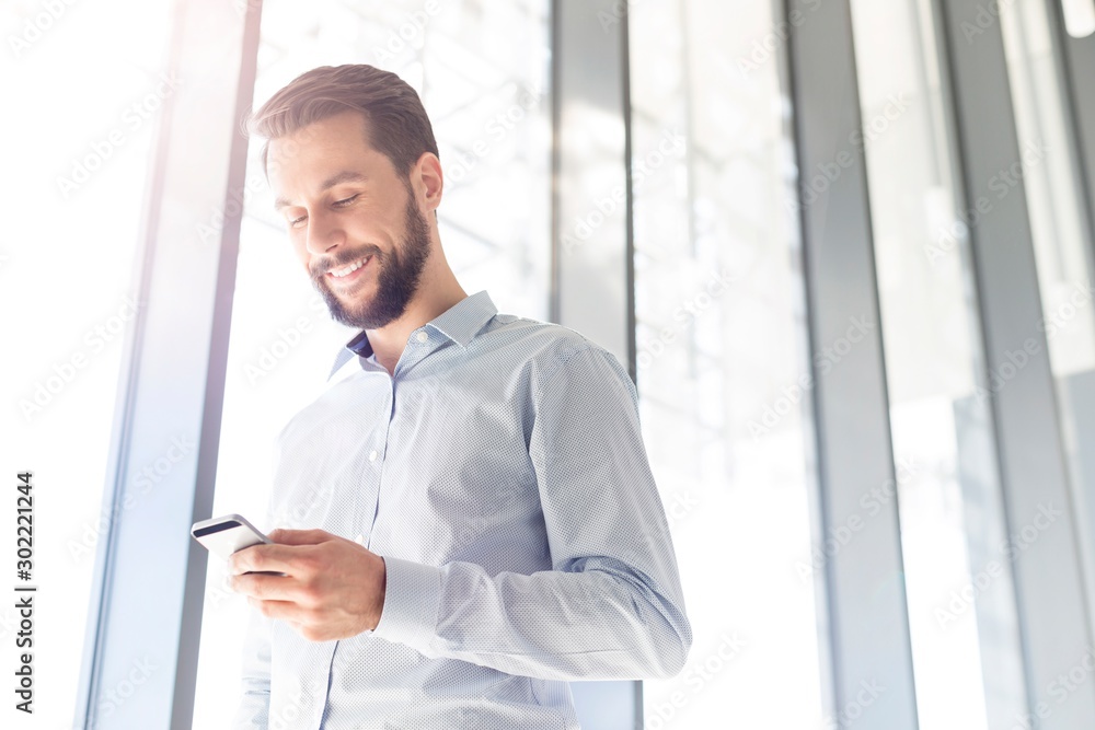 Fototapeta premium Businessman smiling while using smartphone in office