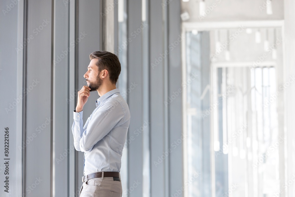 Fototapeta premium Young thoughtful businessman looking in to the window in office