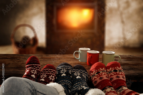 Woolen christmas socks and woman legs on wooden table. Free space for your decoration.Fireplace in home interior with warm orange light of fire.Copy space and winter cold night.Xmas time and gifts.