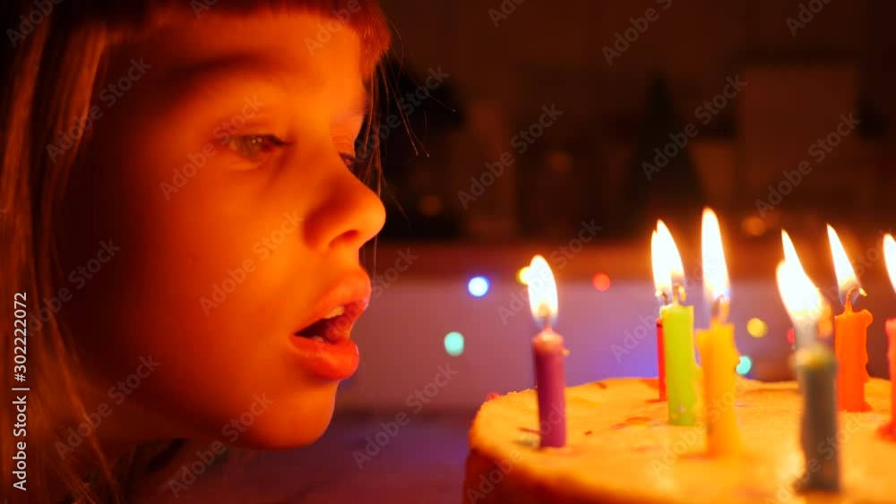Cute little kid girl enjoy blow out candles on birthday cake celebrating at home slow motion