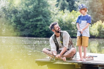 Smiling father looking at son standing on pier while fishing in lake