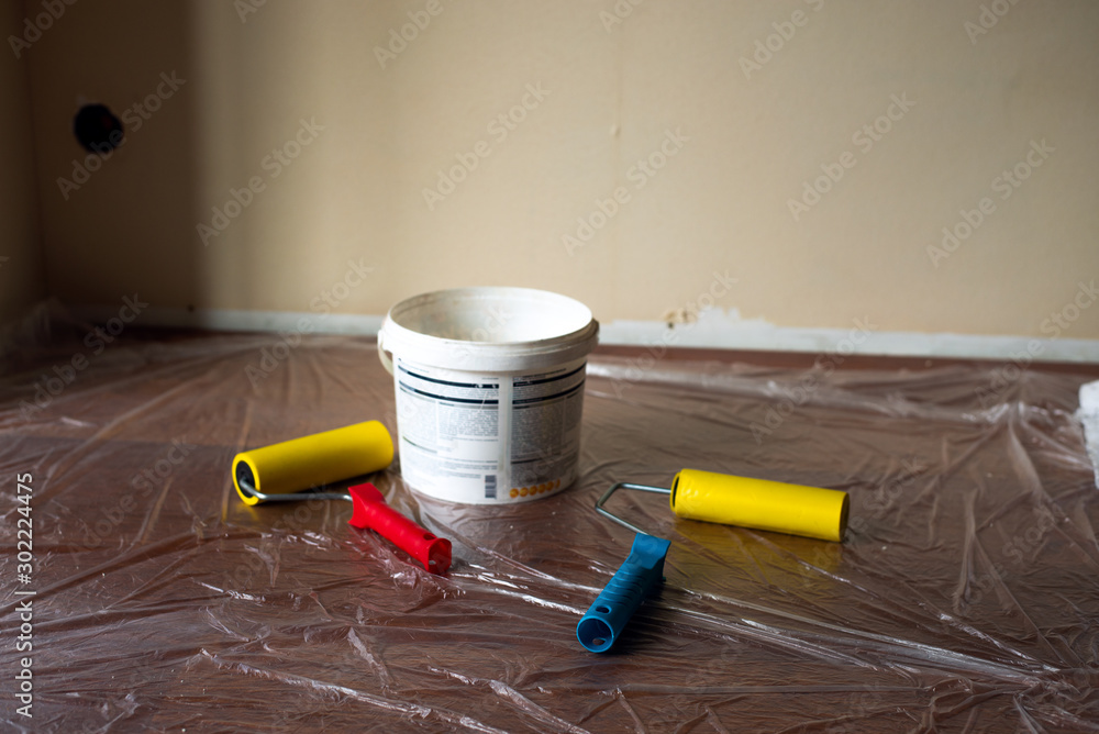 White bucket with paint and wallpaper rollers on the background of oilcloth  on the floor. Room repair Stock Photo | Adobe Stock