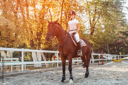 Young jockey girl riding a brown horse in the summer at sunset.