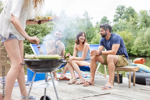 Low section of woman preparing food in barbecue grill with friends on pier